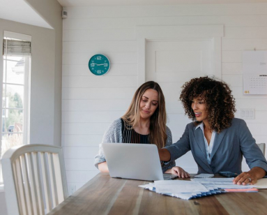 two women looking at website homepage on laptop.